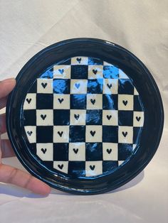 a hand holding a black and white checkered plate with hearts painted on the side