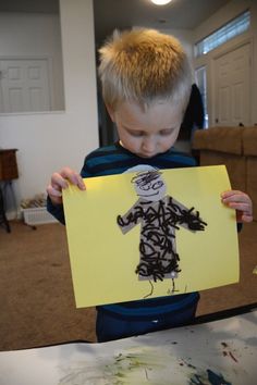 a young boy holding up a piece of paper with a drawing on it