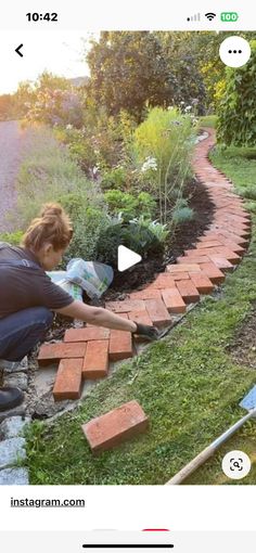 a woman kneeling down next to a brick path in the grass with flowers growing on it