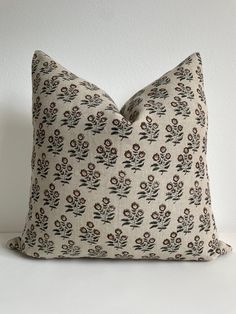 a white pillow with black and red flowers on it, sitting against a white wall