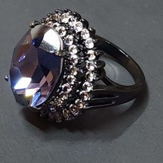 "Add an edgy vibe to your look with our Purple and Black Goth Ring. This statement piece features one large purple (Tanzanite) faceted CZ surrounded with many small clear faceted CZs cubic zirconia set against a black backdrop for a striking contrast. The cocktail ring is designed to make a statement with its unique and intricate details that exude boldness and confidence. Whether you're dressing up for a night out or want to elevate your casual look, our Purple and Black Goth Ring will be the perfect finishing touch to any outfit. Get ready to turn heads and receive compliments with this must-have addition to your jewelry collection. This is a high quality ring, Goth jewelry. Statement ring. Lots of sparkle. The front of the ring is 24mm tall.  The ring band is 2.5mm wide. The purple ston Gothic Party Ring Jewelry, Gothic Party Ring, Elegant Black Amethyst Promise Ring, Elegant Black Crystal Ring For Party, Elegant Purple Crystal Ring For Party, Elegant Purple Crystal Party Ring, Christian Jewelry Necklaces, Black Statement Ring, Purple Tanzanite