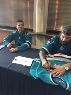 two men sitting at a table signing autographs for the nfl team, one is wearing a green jersey