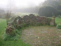 an old stone wall in the middle of a grassy area with plants growing on it