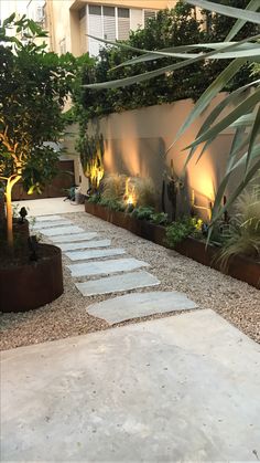 an outdoor garden with stone walkways and lights on the side of the building, surrounded by greenery