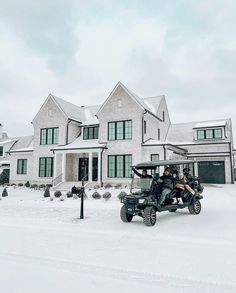 two people riding in a golf cart on the snow covered ground next to a large house