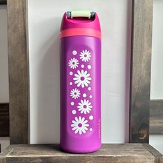 a purple and pink water bottle sitting on top of a wooden shelf next to a white wall