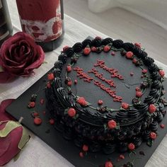 a black cake with red roses on it and a bottle of wine in the background