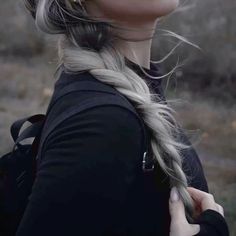 a woman with long grey hair wearing a black top and braided in silver earrings