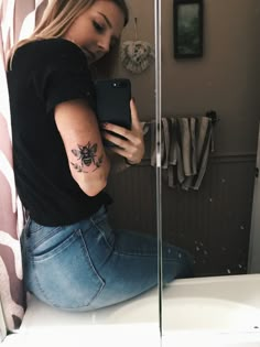 a woman sitting on the edge of a bathroom counter looking at her phone and holding it in her hand