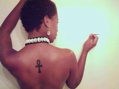 the back of a woman's body with an egyptian cross tattoo on her left side