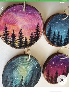 three painted wood slices with trees on them and string hanging from the top, each