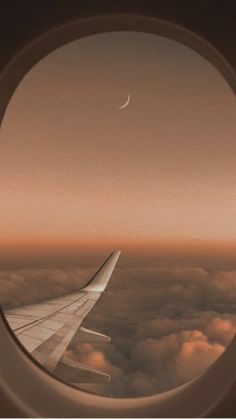 an airplane window looking out at the sky and clouds with a half moon in the distance