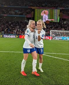 two female soccer players standing on the field with their arms around each other in celebration