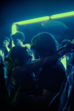 two people hugging each other in front of a crowd at a concert with neon lights