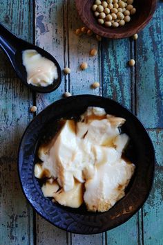 some food is in a black bowl on a blue wooden table with two spoons