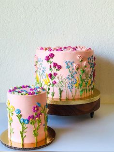 two cakes with flowers painted on them are sitting on a wooden stand next to each other