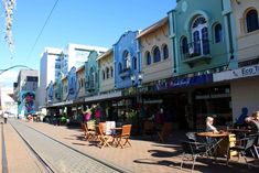 people are sitting at tables on the side walk in front of some shops and buildings