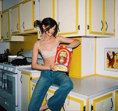 a woman sitting on top of a kitchen counter holding a bag of food in front of her face