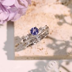 a close up of a ring on a table with flowers in the background and a purple flower next to it