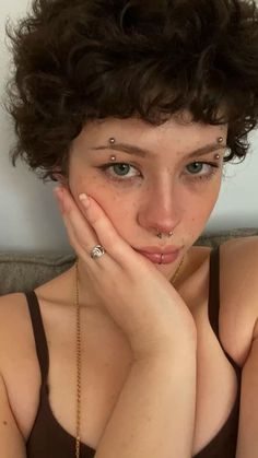 a young woman with piercings on her nose and hand near her face looking at the camera