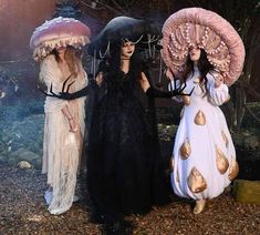 three women dressed in costumes standing next to each other with umbrellas over their heads