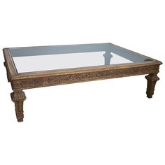 a coffee table with glass top and carved wood frame on the bottom, against a white background