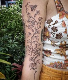 a woman's arm with flowers and leaves on it, in front of some bushes