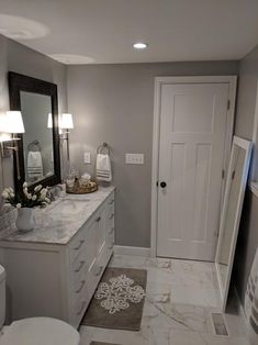 a white bathroom with marble counter tops and gray walls, along with a large mirror on the wall