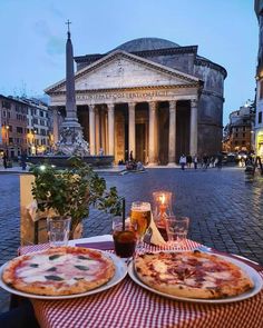 two pizzas sitting on top of a table in front of an old roman building