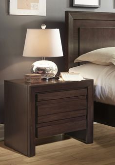 a night stand with a lamp on it next to a bed