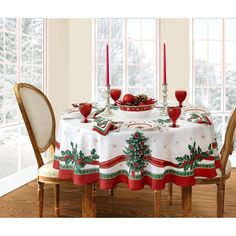 a dining room table set for christmas with red candles and holly wreaths on it