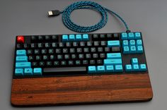 a blue and black computer keyboard sitting on top of a wooden desk next to a usb cable