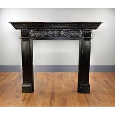 an antique fireplace surround in black wood with carvings on the top and sides, sitting on a hard wood floor