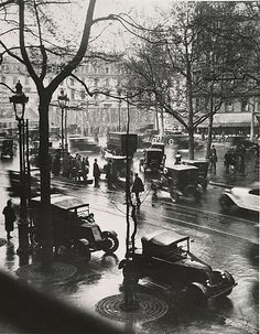 an old black and white photo of cars driving down the street on a rainy day