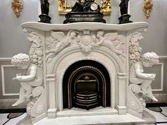 a white fireplace with statues around it and a clock above the fire place on top