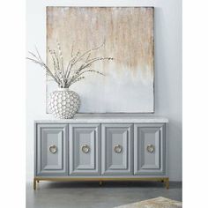 a white vase sitting on top of a gray cabinet next to a painting and rug