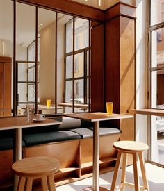 the interior of a restaurant with tables and stools in front of large windows that look out onto an urban street