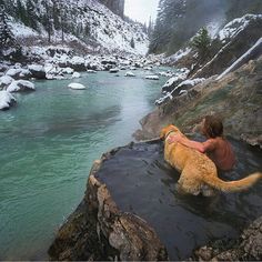 a man and his dog are in the water near a mountain stream that is covered with snow