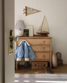 a bedroom with a wooden dresser and blue jeans on it's legs, next to a lamp