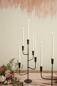 a black candelabra with five white candles on it and flowers in the background