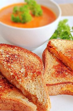 two grilled sandwiches on a white plate with a bowl of soup in the background