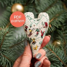 a hand holding a crocheted heart ornament in front of a christmas tree