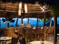 an outdoor dining area with wicker chairs and umbrellas overlooking the ocean at night