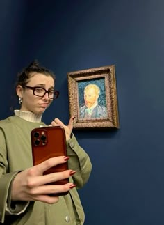 a woman taking a selfie in front of a painting on the wall with her cell phone