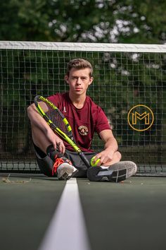 a young man sitting on the tennis court with his racquets and ball