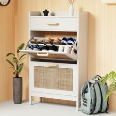 a white cabinet with baskets and shoes on it next to a plant in a pot