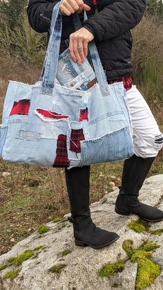 a woman is holding a large bag made out of old jeans and denims, while standing on top of a rock