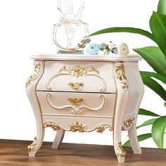 an ornate white and gold chest of drawers with flowers on top, next to a potted plant