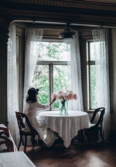 a woman sitting at a table in front of a window with pink flowers on it