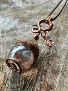 "This pendant is made using copper wire, fancifully looped through an acorn cap and swirling to hold a marble. It is accented with a Swarovski bicone bead. It's overall dimensions are 1.75\" long and 1\" at its widest point featuring a 16mm marble. It is on a leather cord tied with slip knots for an adjustable length.  We recommend removing this piece before showering or sleeping as it incorporates natural elements that should be treated with care." Nature-inspired Necklace With Natural Stones And Copper Wire, Fairy Acorn Necklace, Gold Acorn Necklace, Nature-inspired Copper Wire Pendant Jewelry, Acorn Crystal Necklace, Acorn Necklace, Cord Ties, Natural Elements, Copper Wire